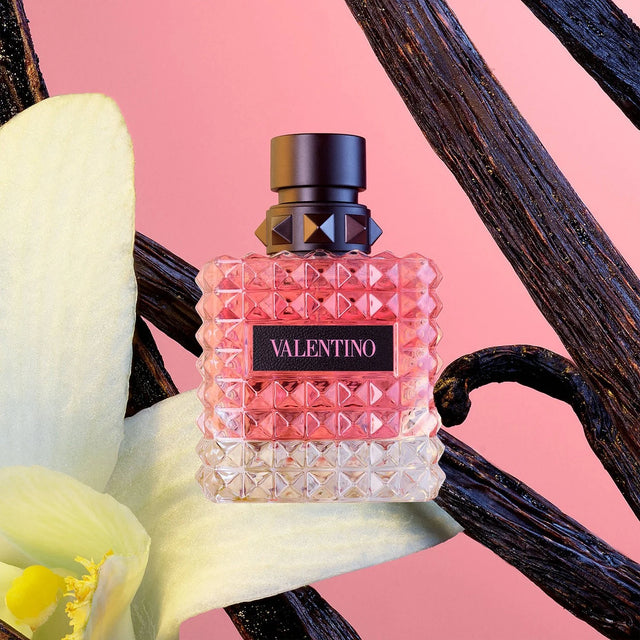 Valentino perfume bottle with flowers and vanilla beans on a pink background