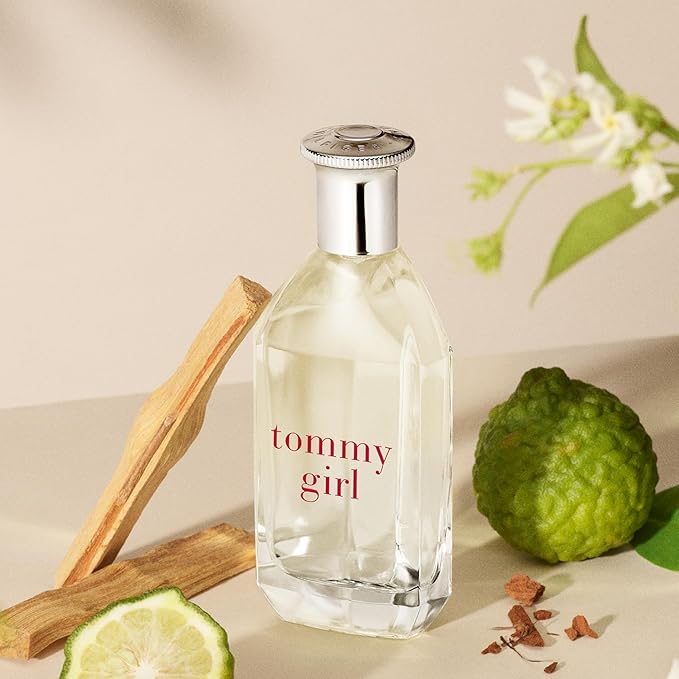 Tommy Girl perfume bottle with a wooden stick and green fruit on a beige background