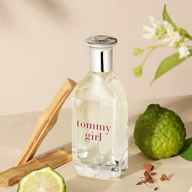 Tommy Girl perfume bottle with a wooden stick and green fruit on a beige background