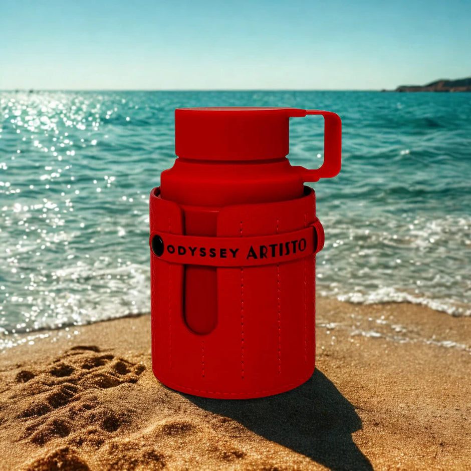 Red thermos with 'Odyssey Artista' branding on a sandy beach with ocean in the background