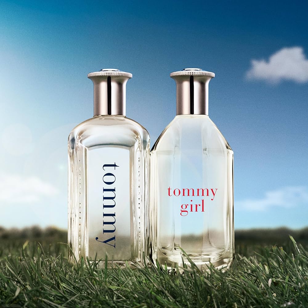 Two perfume bottles labeled 'tommy' and 'tommy girl' on grass with a blue sky background