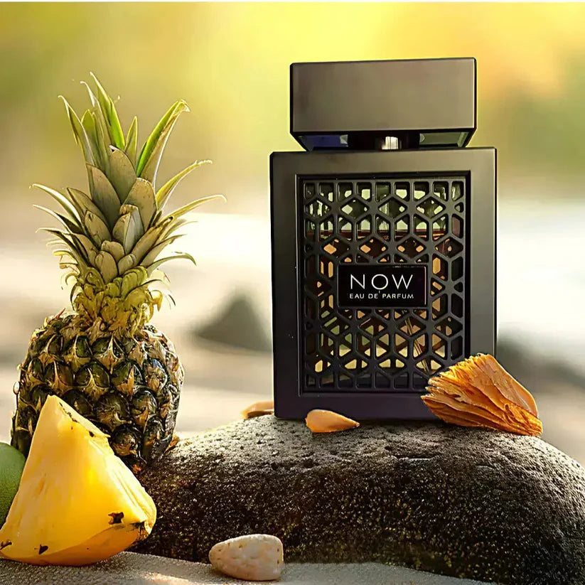 Black perfume bottle labeled 'NOW' with a pineapple and leaf on a textured surface.