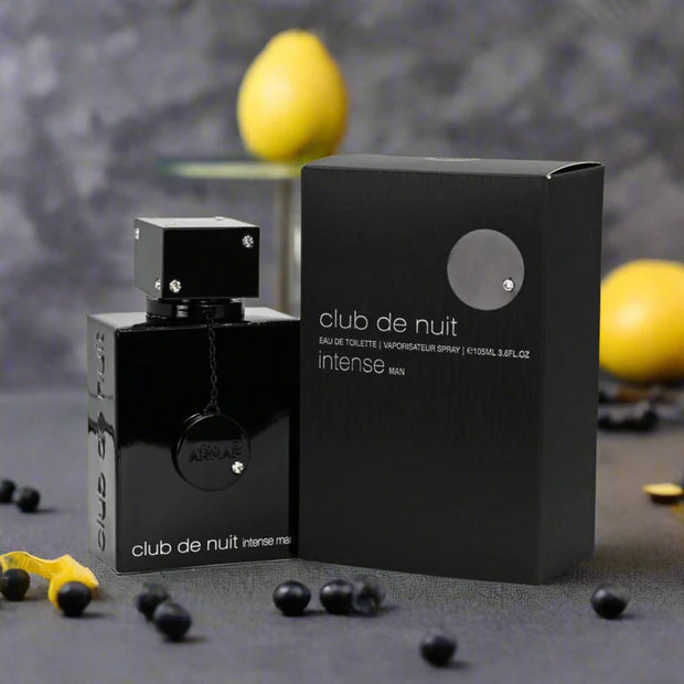 Black perfume bottle and packaging labeled 'club de nuit intense' on a dark surface with lemons in the background.