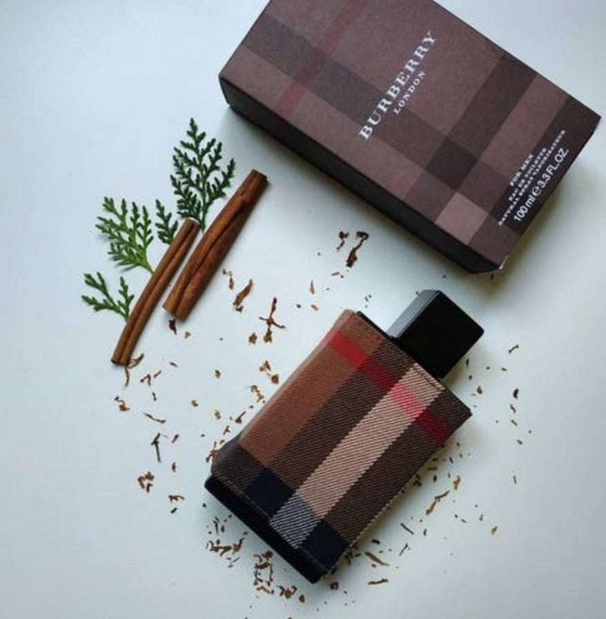 Burberry perfume bottle and packaging with cinnamon sticks and green leaves on a light background