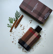 Burberry perfume bottle and packaging with cinnamon sticks and green leaves on a light background