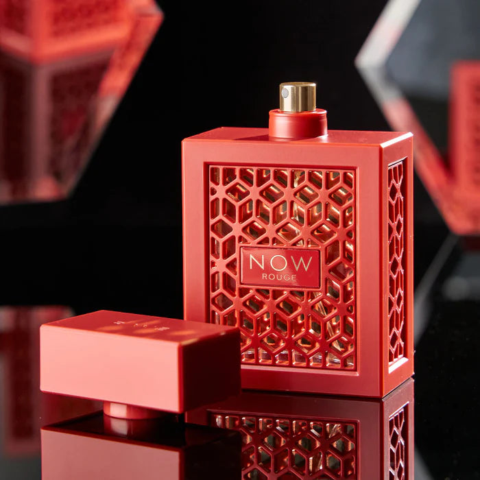 Red perfume bottle with geometric design and 'NOW Rouge' label on a reflective surface.